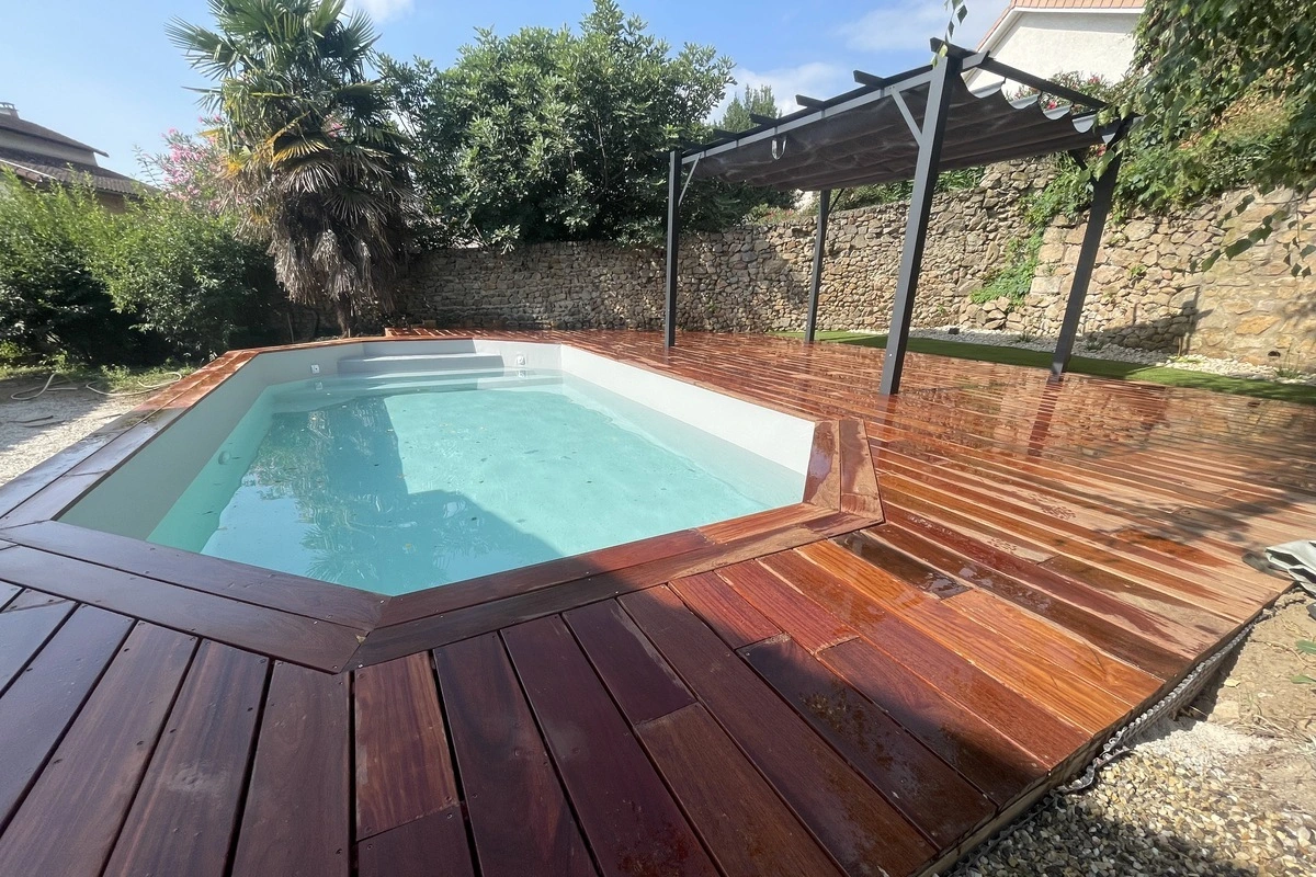 Piscine entourée d'une terrasse en bois exotique, illustrant un aménagement extérieur complet et esthétique.