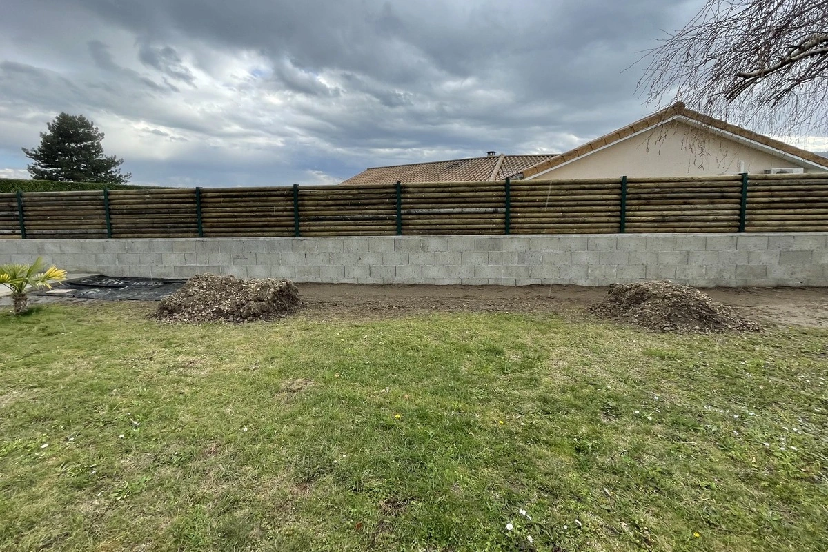 Clôture en bois sur un mur de soutènement en béton, montrant un aménagement paysager réalisé par un paysagiste pour améliorer la sécurité et l'esthétique du jardin.